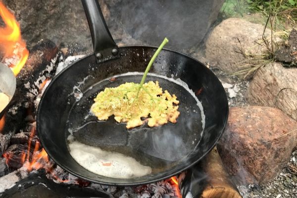 Elderflowers fried on a campfire pan becoming beautiful elderflower pancakes.